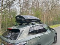 Beispiel: Thule Touring "M" Dachbox auf einem grünen Auto, parkt an einer Straße mit Bäumen im Hintergrund.