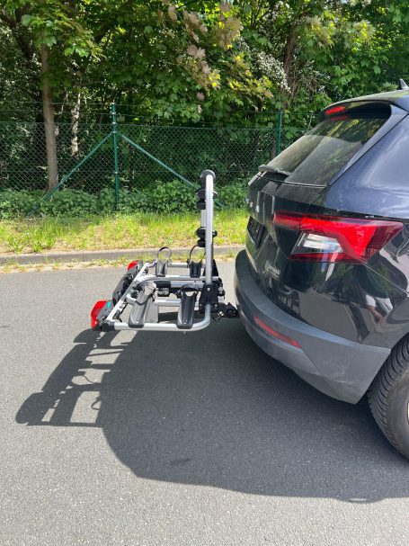 Fahrradträger montiert am Heck eines schwarzen Autos auf einer gepflasterten Straße.