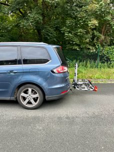 Blauer SUV mit einem Fahrradträger am Heck, unbefestigter Untergrund im Hintergrund.