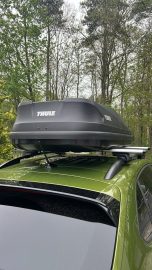 Beispiel: Thule Motion "L" Dachbox auf einem grünen Auto, platziert auf einem gepolsterten Dachträger.