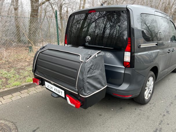 Thule Heckbox Onto Ein grauer Lieferwagen mit einem abgedeckten Gepäckträger auf der Rückseite.
