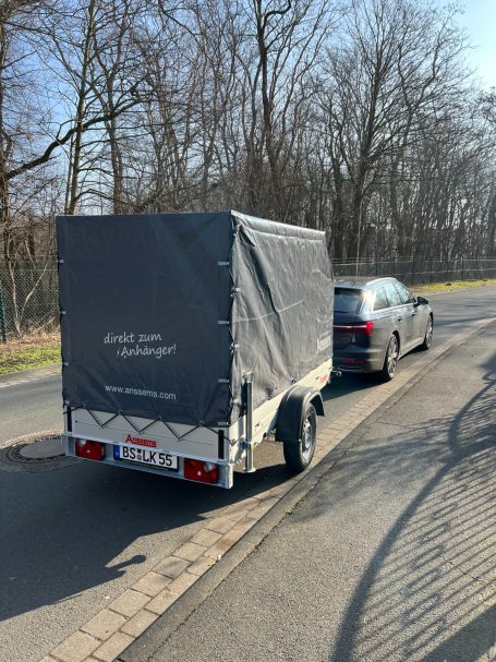 Anhänger: Anssems GTB | 750kg Ein Anhänger mit Plane steht neben einem schwarzen Auto auf einer Straße.
