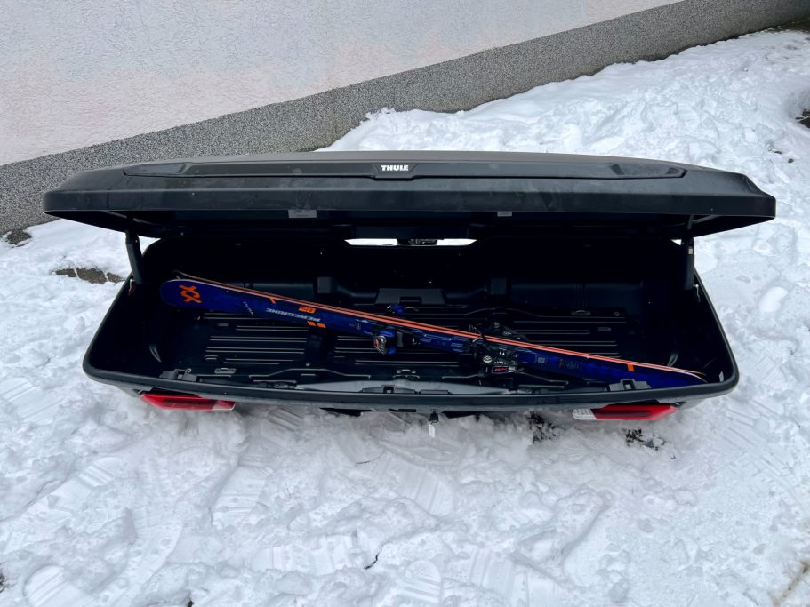 Schwarzer Kofferraum im Schnee mit einem langen, blauen und orangefarbenen Gegenstand.