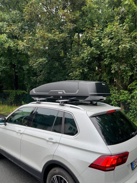 Ein weißer SUV mit einem Dachgepäckträger und einer schwarzen Gepäckbox.