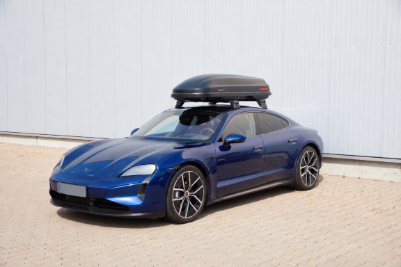 Blauer Sportwagen mit Dachbox steht auf einem gepflasterten Platz.