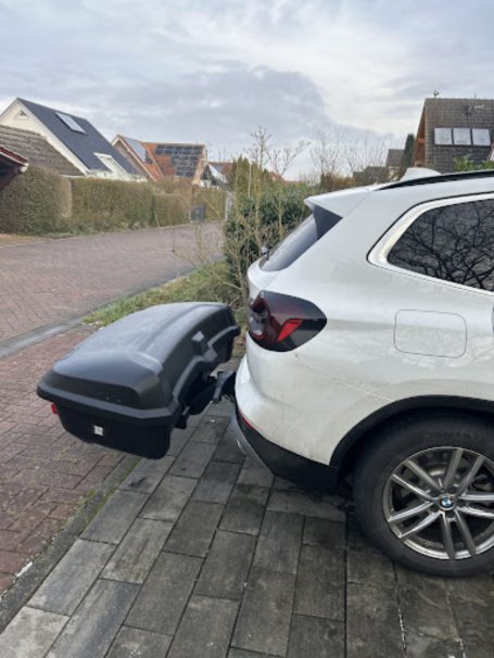 Weißes SUV mit einem schwarzen Anhänger, geparkt in einer Wohngegend.