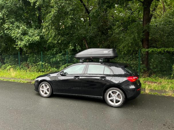 Schwarzer Wagen mit Dachbox, geparkt an einer grünen Straße.