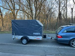 Ein grauer Anhänger, der an einem blauen Auto auf einer Straße geparkt ist.