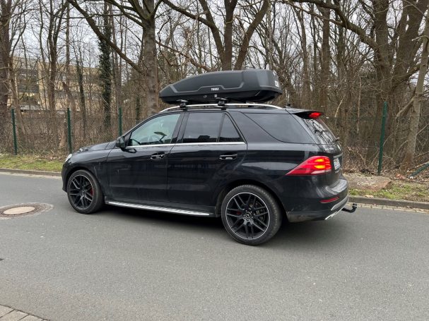 Schwarzer SUV mit Dachgepäckträger, auf einer Straße nahe Bäumen geparkt.