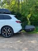 Thule Heckbox Arcos Gr. L Weiße SUV mit Dachgepäckträger und Anhänger, geparkt in einer grünen Umgebung.