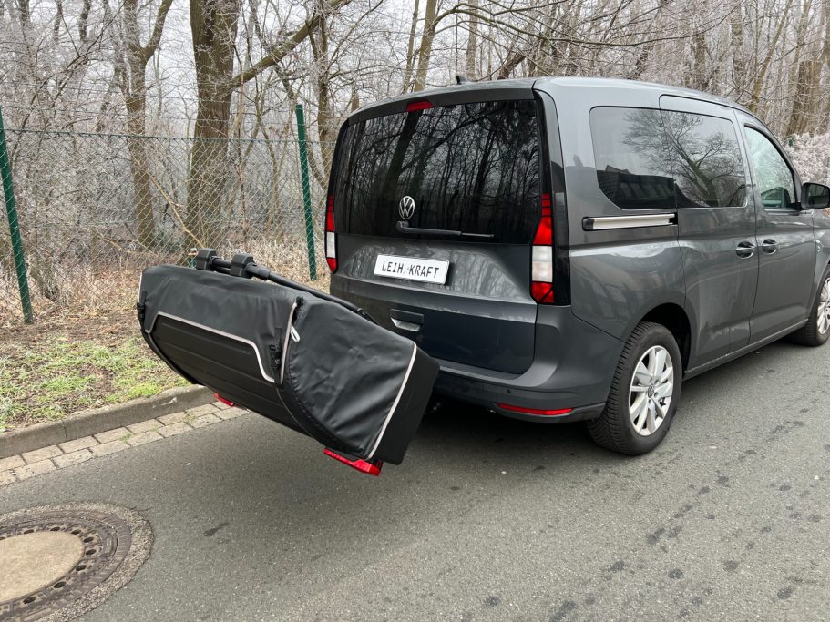 Transporter mit einem schwarzen Sack auf der Rückseite, parkt an einer Straße.