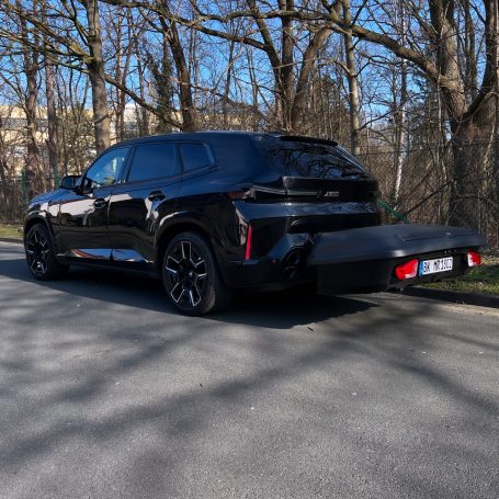 Schwarzes SUV parkt auf einer Straße, umgeben von Bäumen und Wohngebäuden.