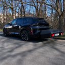 Thule Heckbox Arcos Gr. L Schwarzer SUV parkt an einer Straße, umgeben von Bäumen.