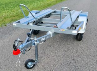 Anhänger mit Metallrahmen und einem Rad an der Vorderseite, auf asphaltierter Straße.