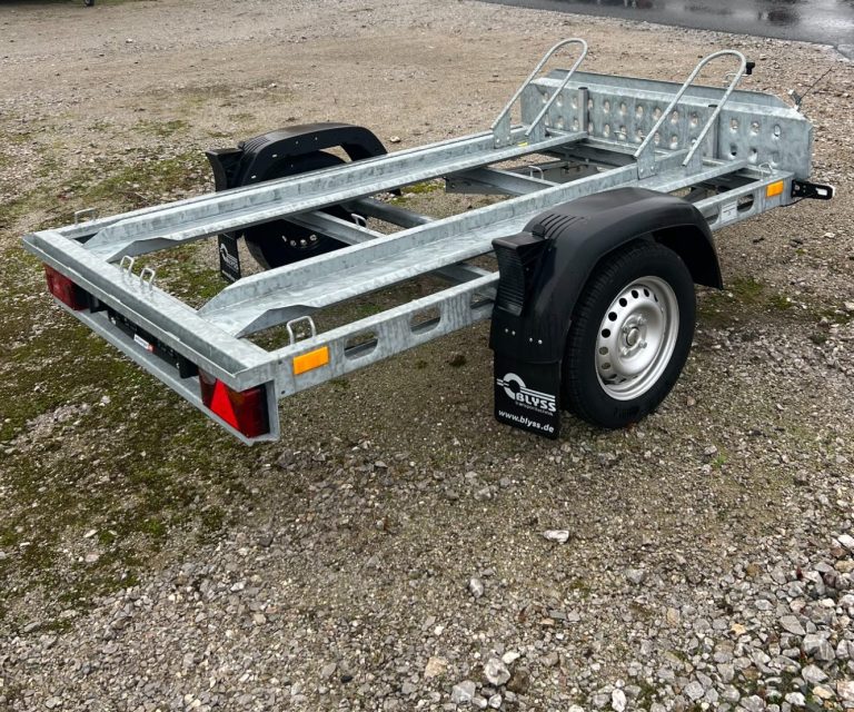 Anhänger mit grauem Cover steht neben einem schwarzen Auto auf der Straße.