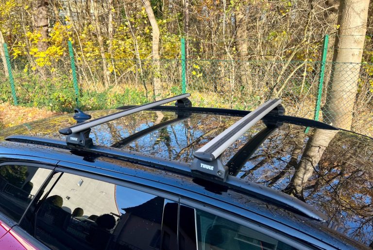 Geeignet für Fahrzeuge mit integrierter Dachreling "Flush-Rail" Dachträger auf einem schwarzen Auto, Umgebung mit Bäumen und Zaun im Hintergrund.