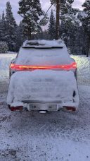 Thule Heckbox Onto Ein Fahrzeug im Schnee, mit einer schneebedeckten Rückseite und leuchtenden Rücklichtern.