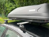 Dachbox mit dem Thule Fixpoint-System Dachbox auf dem Auto, montiert auf einem Dachträger, bei bewölktem Wetter.