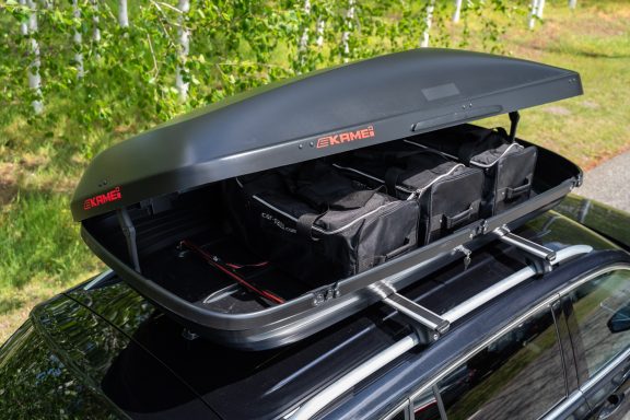 Dachbox auf einem Auto, geöffnet und mit schwarzen Taschen gefüllt.