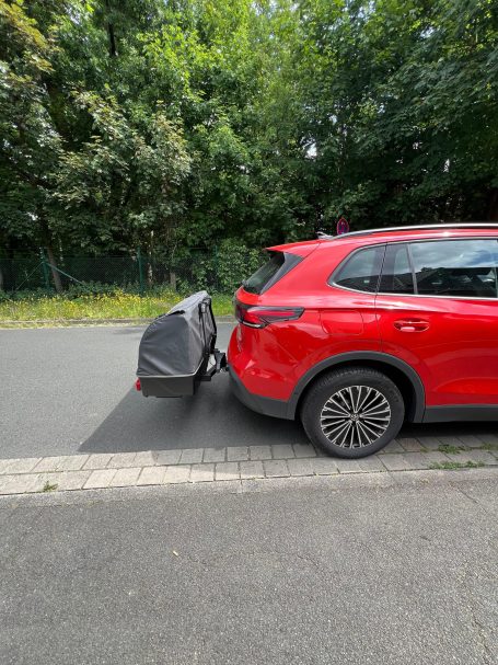 Roter SUV mit einem angeschlossenen Fahrradträger auf der Straße.