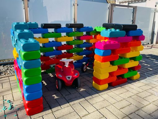 Bunte Bauklötze bilden eine Spielstruktur mit einem roten Spielauto daneben.