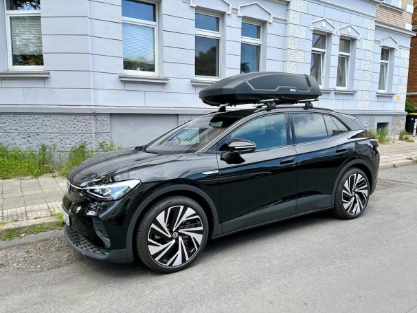 Schwarzes Auto mit Dachbox, geparkt vor einem historischen Gebäude.