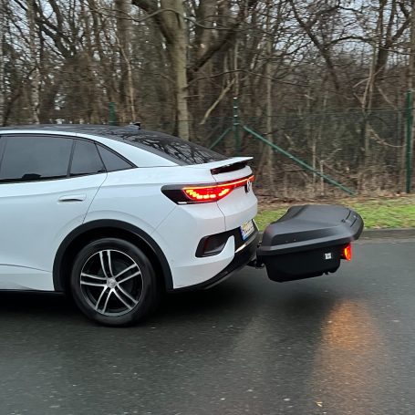 Weißes Auto mit Anhängerkupplung und abnehmbarem Anhänger auf einer Straße.