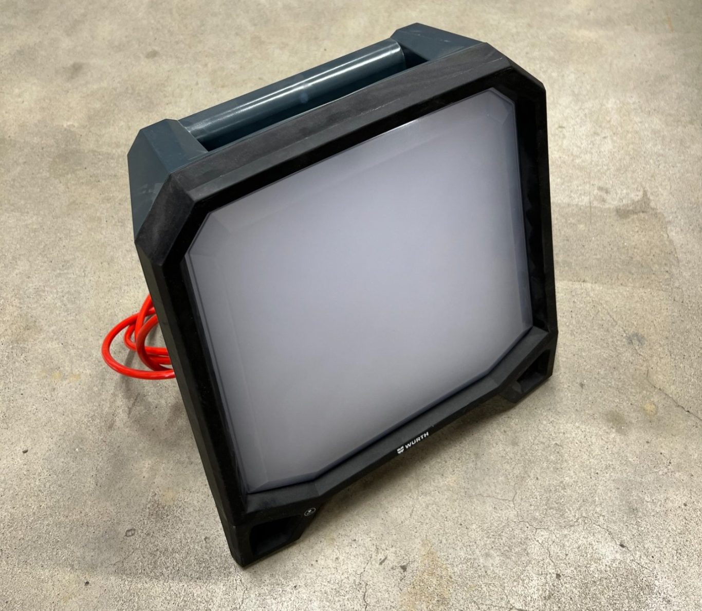 Tragbare LED-Leuchte mit schwarzem Gehäuse und rotem Kabel.