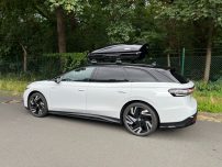 Beispiel: Thule Touring "M" Weißer Kombi mit Dachbox steht an einem ruhigen Straßenrand, umgeben von Bäumen.